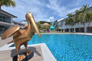 A swimming pool with a large golden pelican sculpture in the foreground and a blue sculpture in the background.