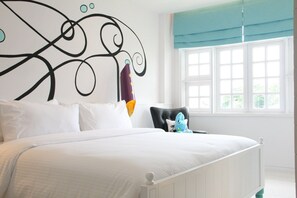 A bedroom with a large bed, a decorative headboard, a window with blinds, and a plush toy on the nightstand.