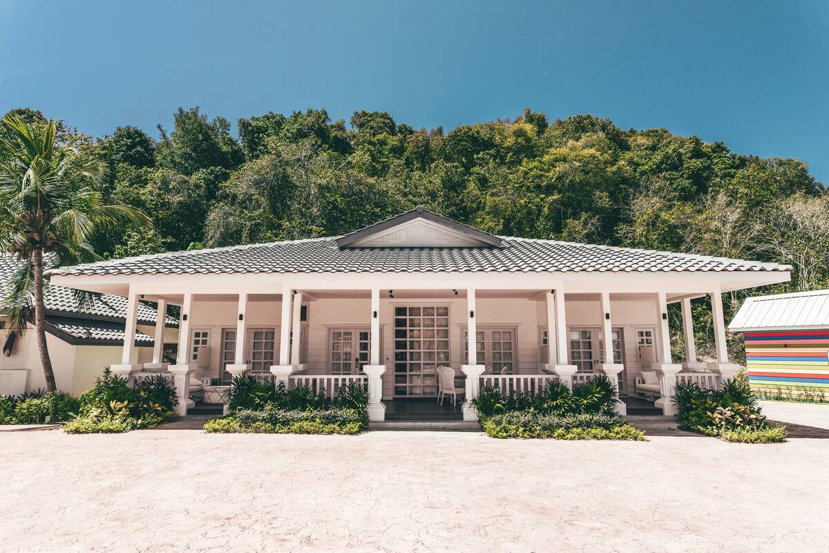 A white building with a tiled roof, columns, and a covered porch with chairs.