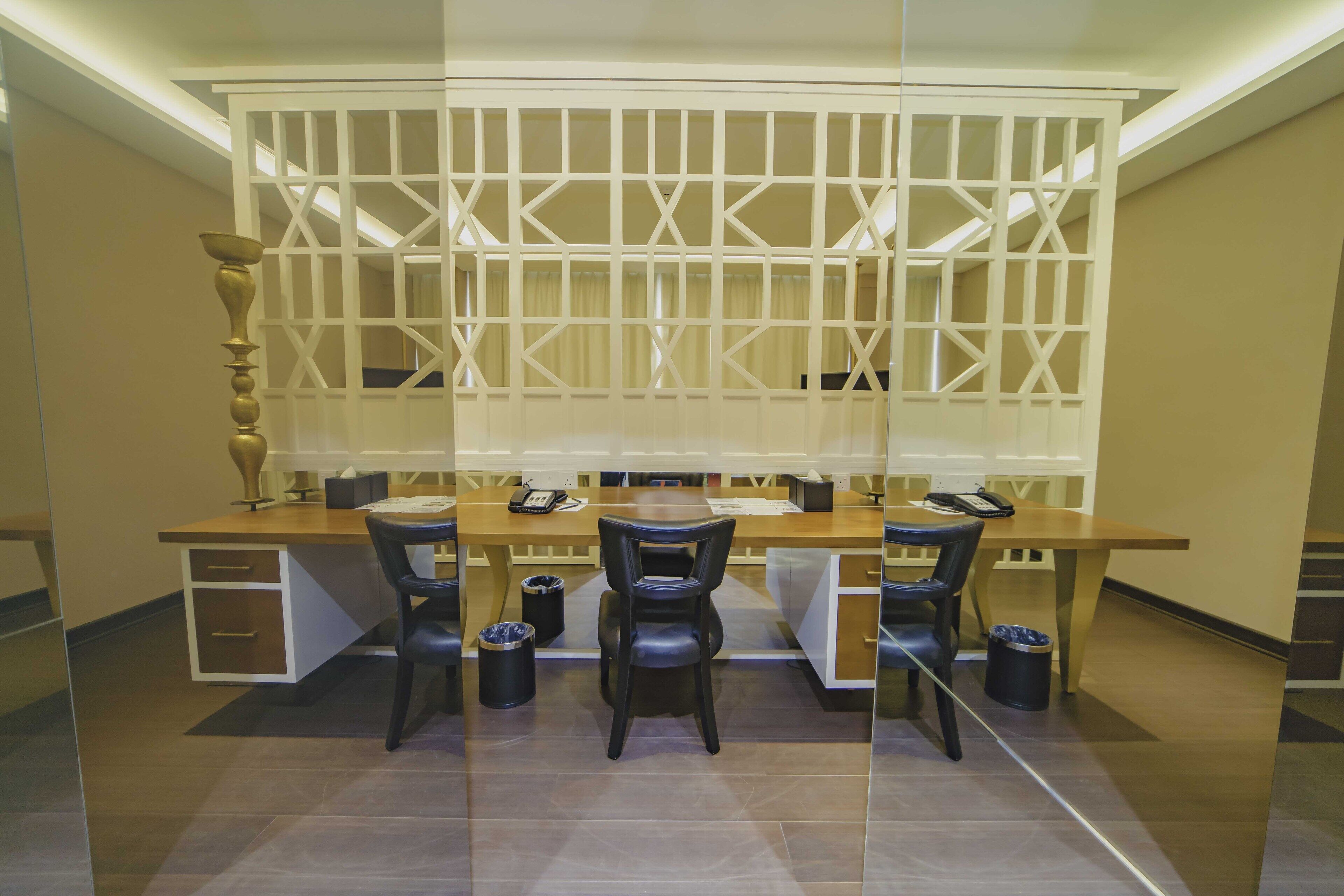 A modern office space with a long desk, two black chairs, a telephone, and a decorative vase.
