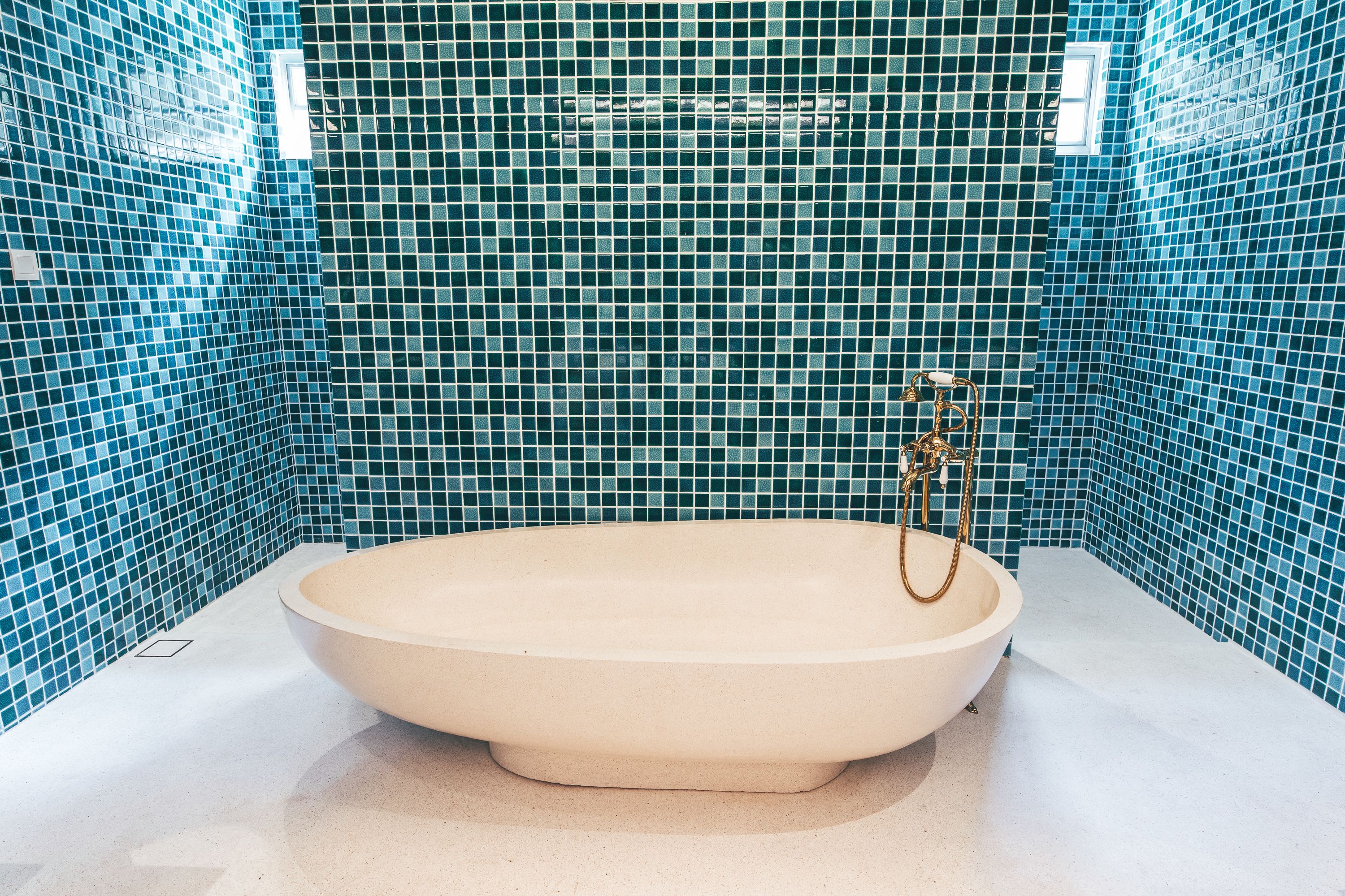 A bathtub with a gold faucet in a bathroom with blue mosaic tile walls.