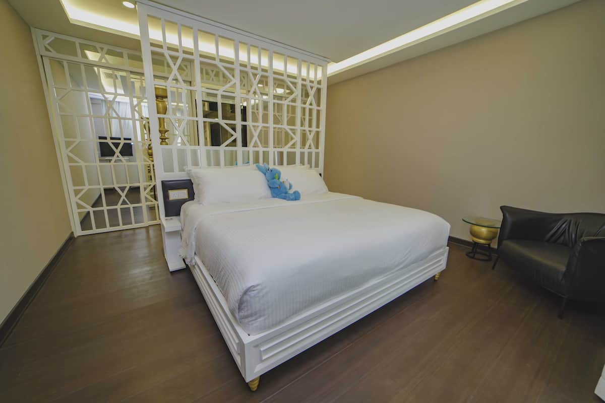 A bedroom with a large bed, a white headboard, a black leather sofa, and a decorative white partition.