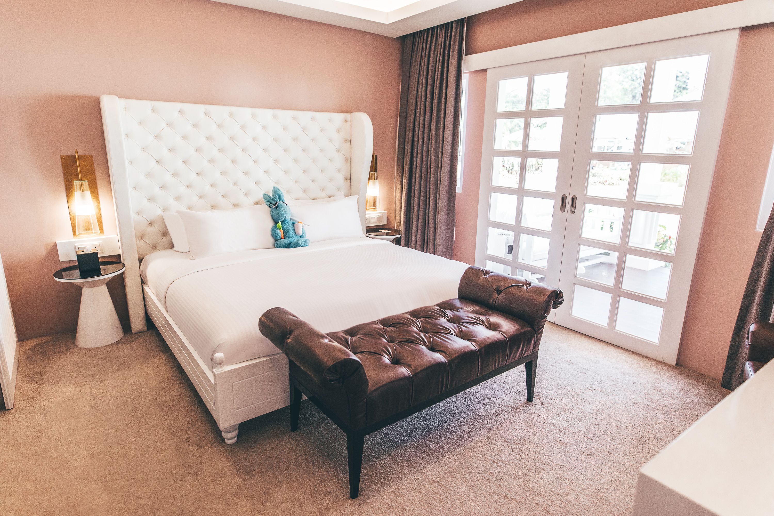 A bedroom with a large bed, a bench, two bedside tables, and a sliding glass door.