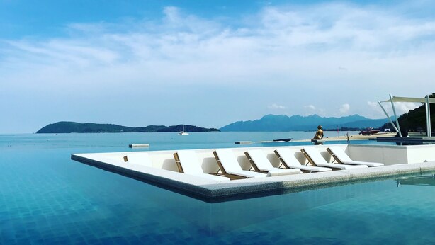 An infinity pool with lounge chairs, a beach area, and a view of distant mountains. - Dash Resort Langkawi (Langkawi)