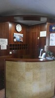 Un mostrador de recepción con un reloj, un cuadro enmarcado y un cartel que indica los horarios de registro de entrada y salida.