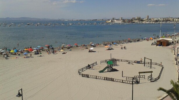 Une plage avec une aire de jeux, des parasols et une vue sur la mer et les bâtiments qui se dressent au loin.