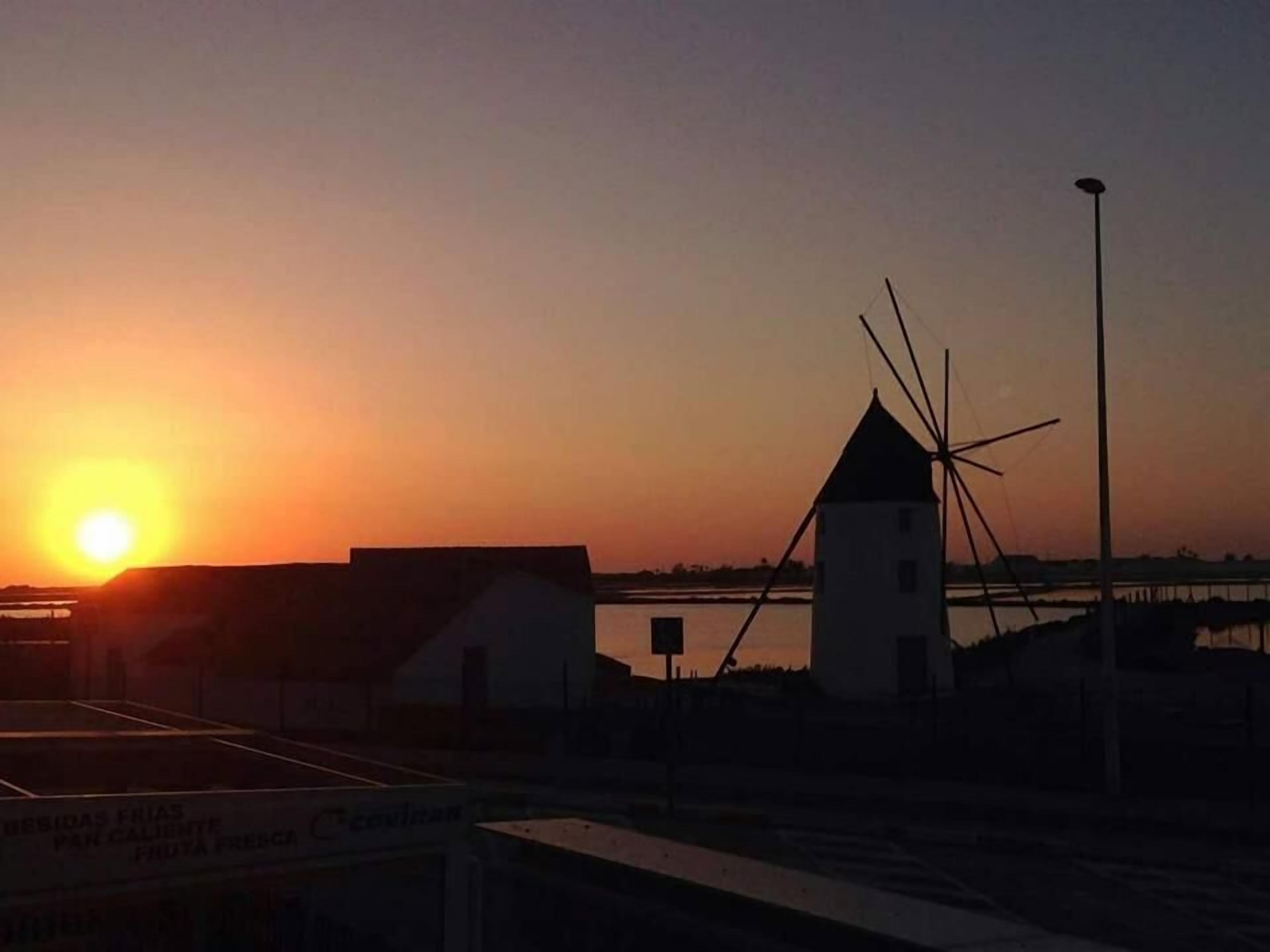 A sunset with a windmill and a building in the foreground.