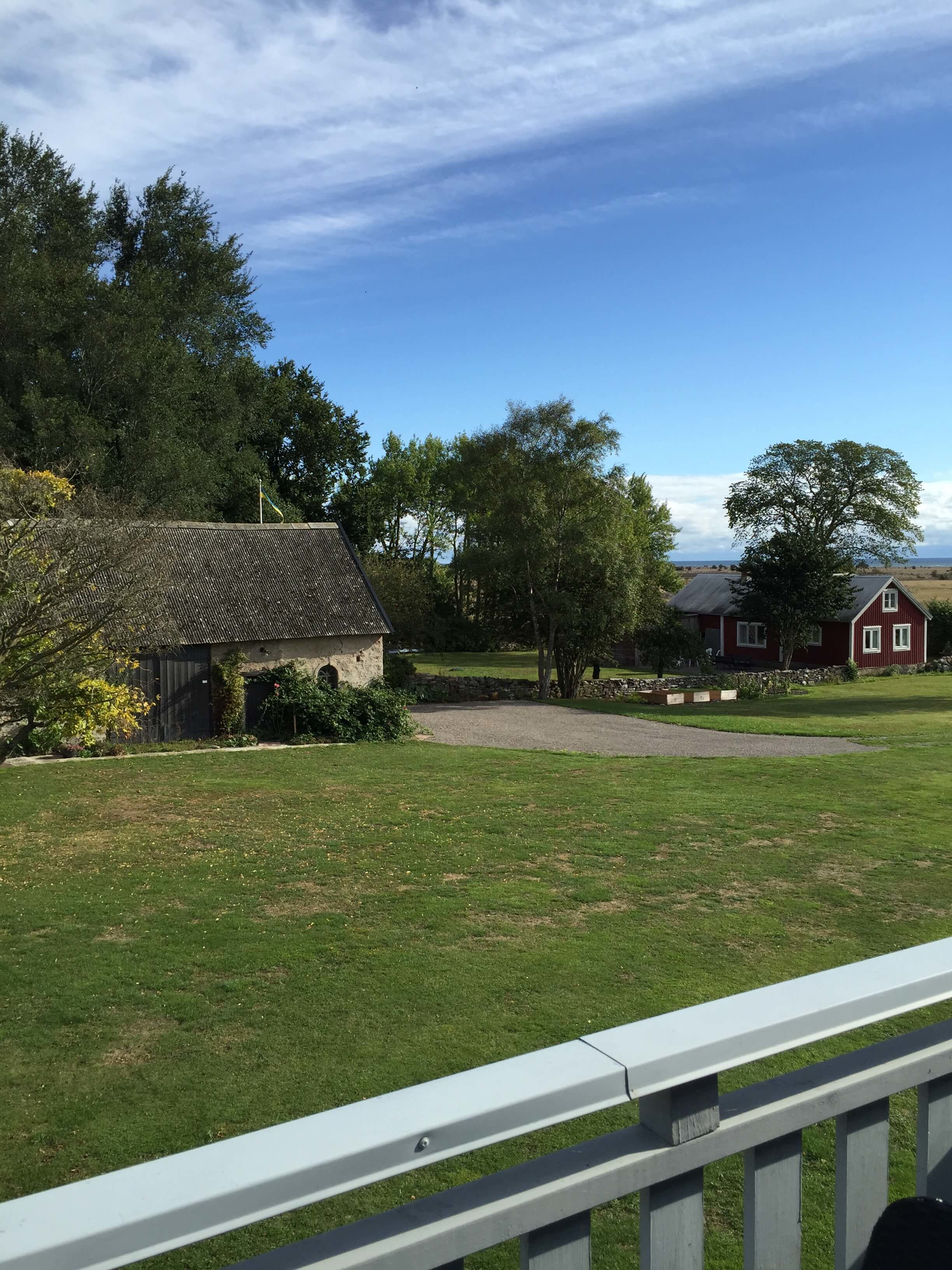 A rural landscape with a small stone building, a red house, and a grassy field.