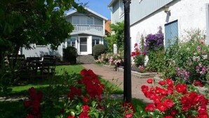 Un edificio residencial con un porche delantero, un jardín con flores rojas y un banco de madera.