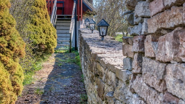 Un muro de piedra con una escalera de madera que conduce a un edificio rojo con techo de paja.