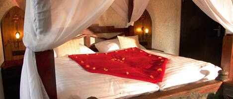 Una cama con dosel, ropa de cama blanca y una colcha roja.