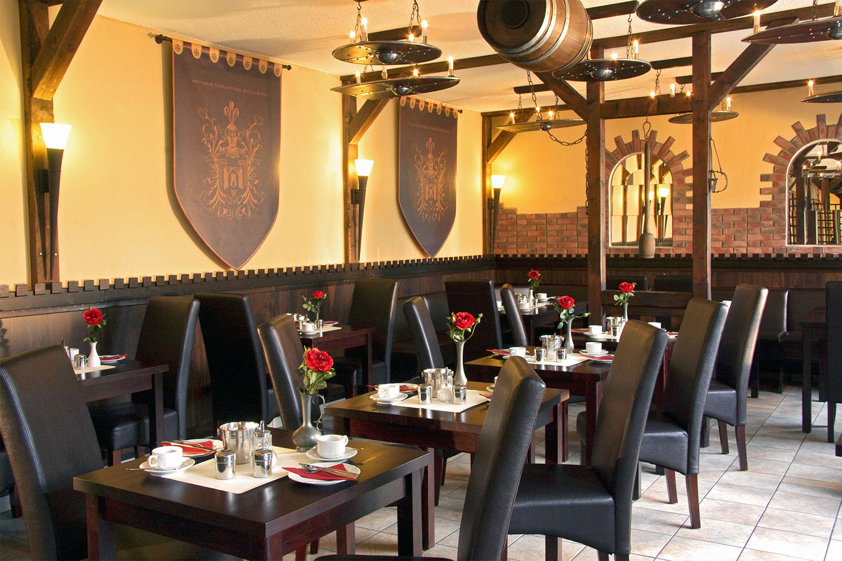 Un restaurant avec des tables en bois, des chaises noires et des roses rouges disposées sur les tables.