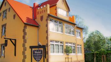 A two-story building with a red roof and yellow walls, featuring a sign that reads "Hotel."