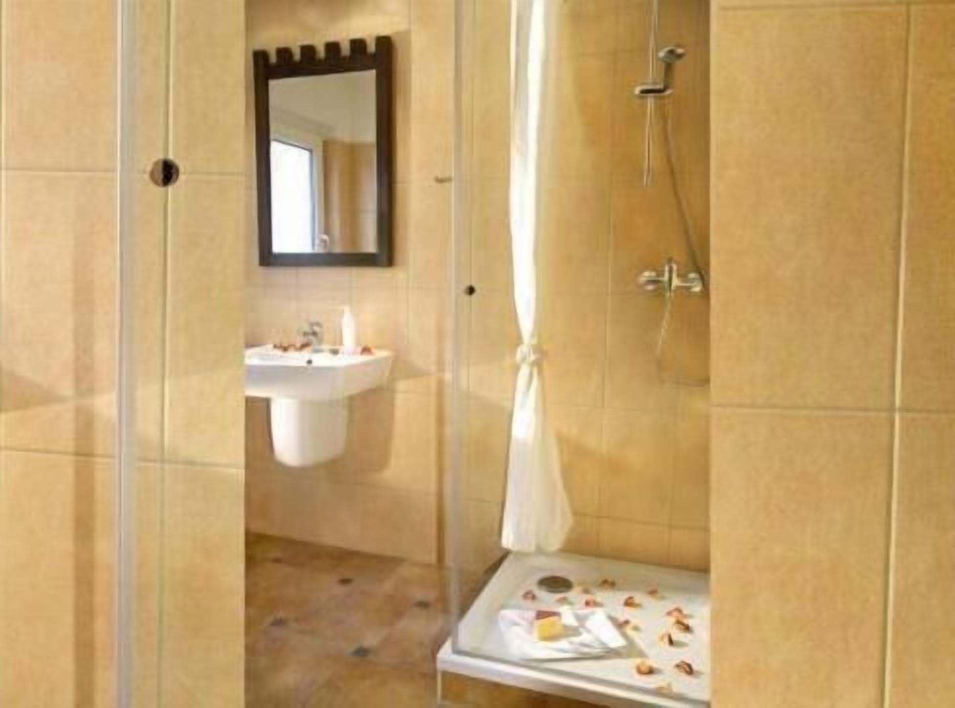 A bathroom with a sink, mirror, shower, and a small table with toiletries.