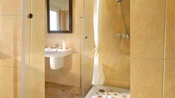 A bathroom with a sink, mirror, shower, and a small table with toiletries.