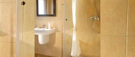 A bathroom with a sink, mirror, shower, and a small table with toiletries.