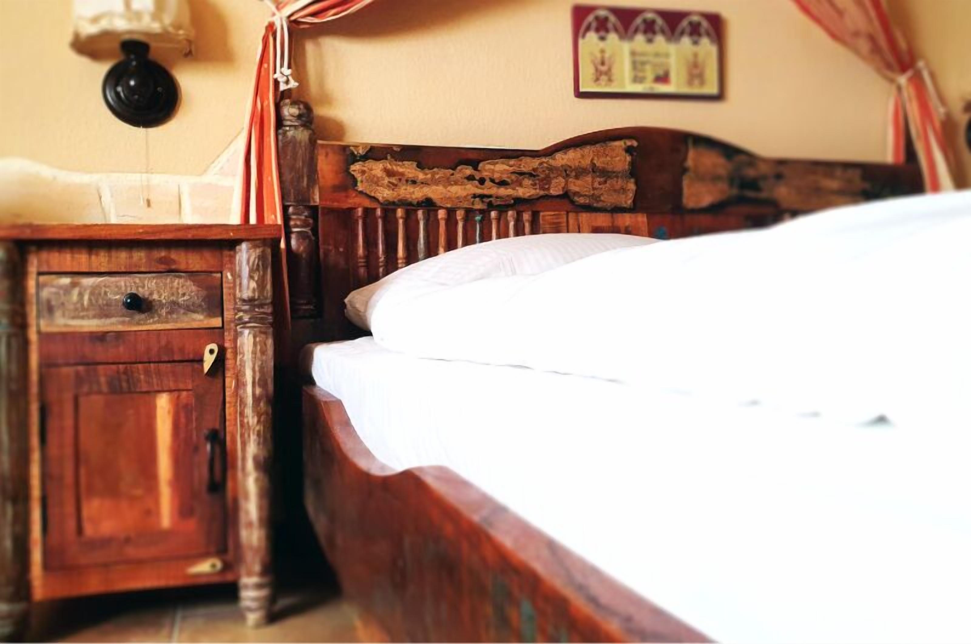 A wooden bed with a headboard, a wooden nightstand with a drawer, and a wall-mounted lamp.