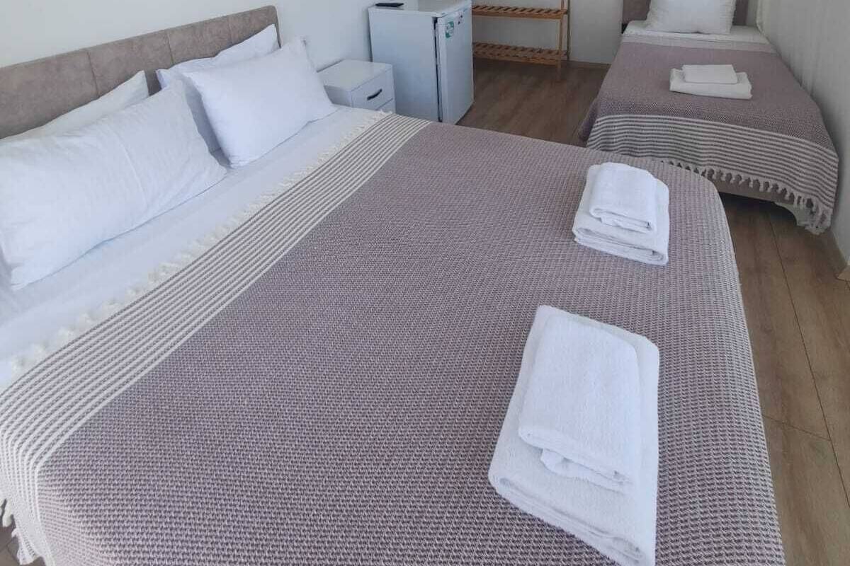 Habitación de hotel con dos camas, una mesita, una silla, un televisor montado en la pared y un aire acondicionado.