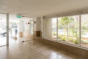 A spacious lobby with a large window, a door leading outside, and a visible exit sign. - Sea N' Rent - 23 Shderot Bialik (Ramat Hasharon)
