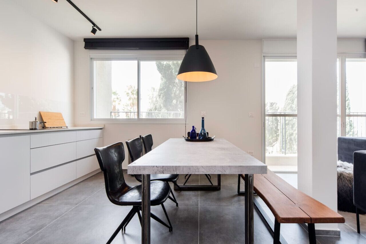 Et moderne køkken med bordplade i marmor, sorte stole, en træbænk og en hængende lampe.