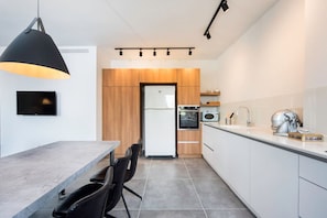 A modern kitchen with a dining area, a TV mounted on the wall, and a refrigerator. - Sea N' Rent - 23 Shderot Bialik (Ramat Hasharon)