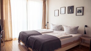 A double bed with striped bedding, a wooden floor, and a window with patterned curtains. - Grafschaft Kloster Zinna (Jueterbog)