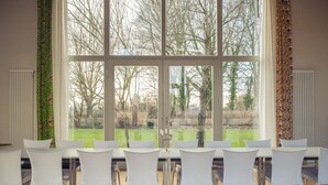 A dining area with a large window, white chairs, and a table. - Grafschaft Kloster Zinna (Jueterbog)