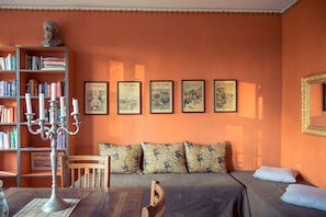 A cozy room with a bookshelf, a candelabra, a sofa with patterned cushions, and a bed with a blue pillow. - Grafschaft Kloster Zinna (Jueterbog)