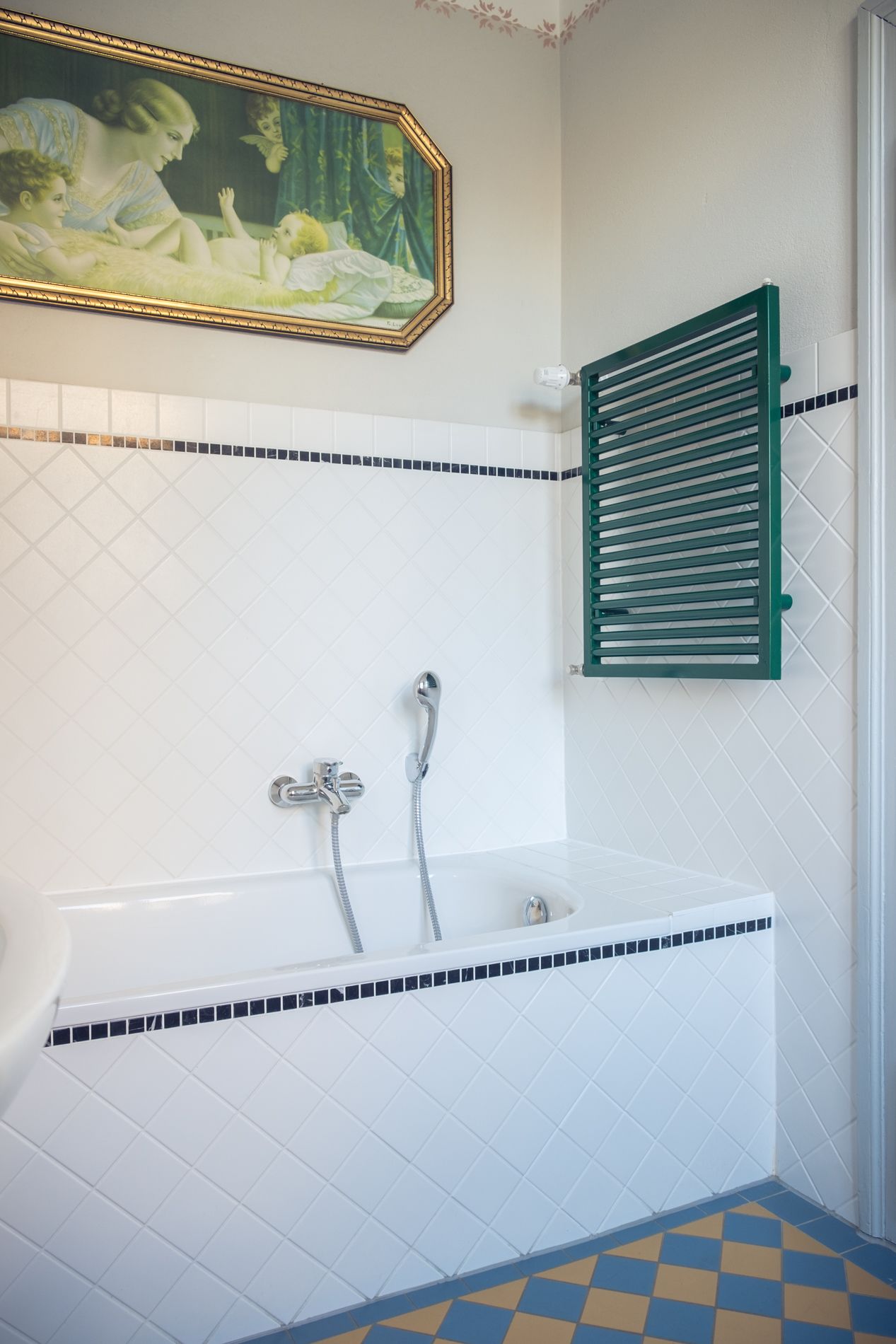 A bathroom with a white bathtub, a green towel rack, and a painting above the tub.