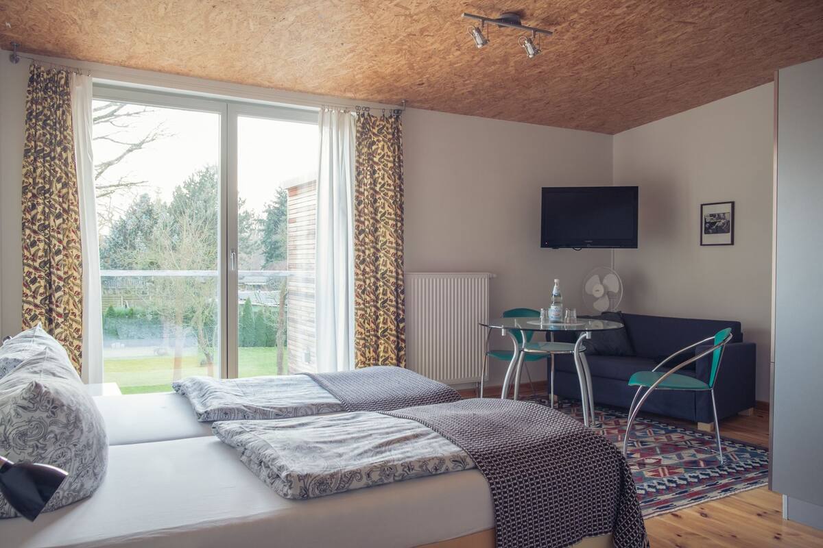 A room with a bed, a table with chairs, a TV, and a view of the outdoors.