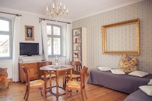 A cozy living room with a dining table, chairs, a sofa, a bookshelf, and a television. - Grafschaft Kloster Zinna (Jueterbog)