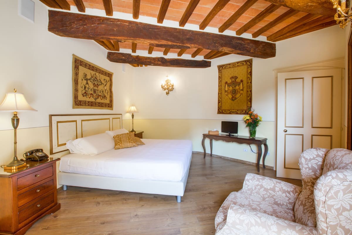 Een slaapkamer met een bed, nachtlampjes, een houten dressoir, een bureau met een computer en een stoel.