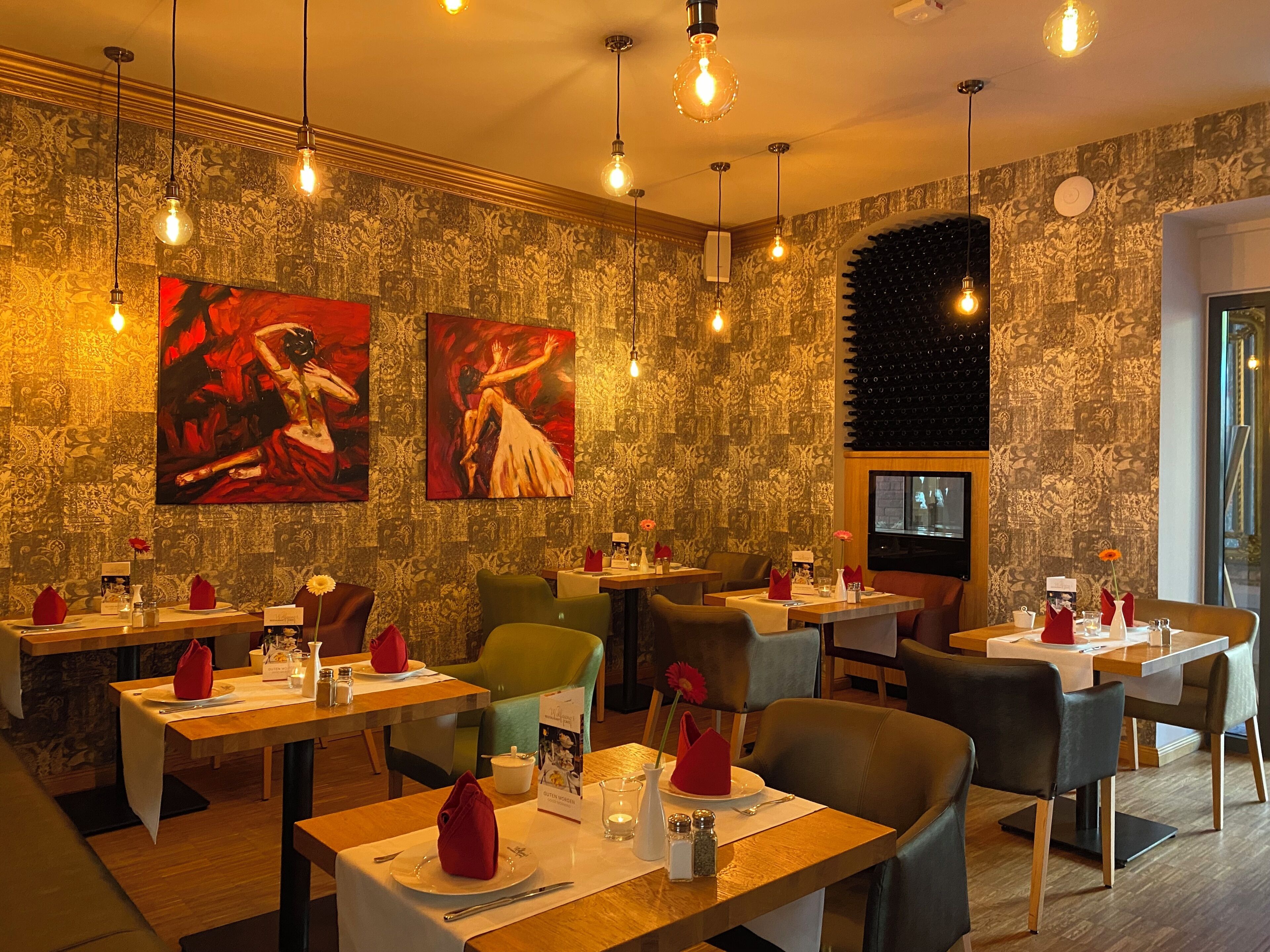 A restaurant with patterned wallpaper, red and white paintings, and tables set with red napkins and menus.