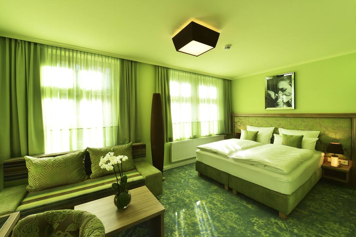 A hotel room with a bed, a sofa, a coffee table, and a large window with curtains.