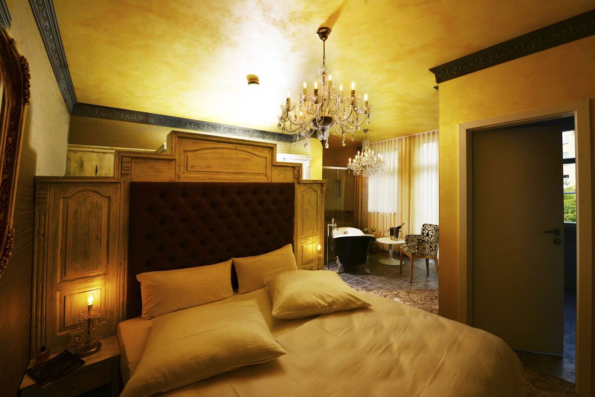 A large bed with a tufted headboard, a chandelier, and a classic design.