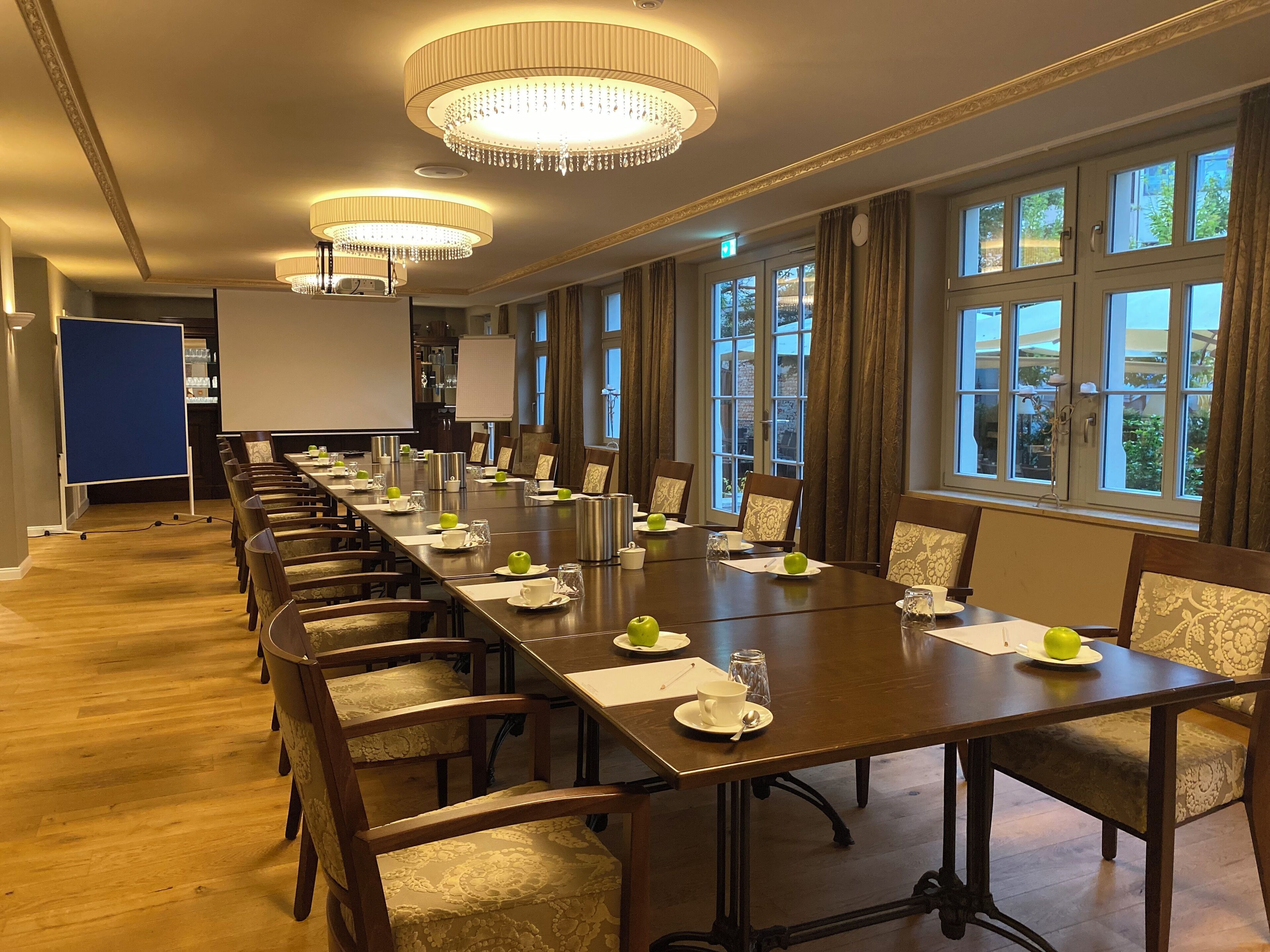 Ein Konferenzraum mit einem langen Tisch, Stühlen und einer Projektionsleinwand.