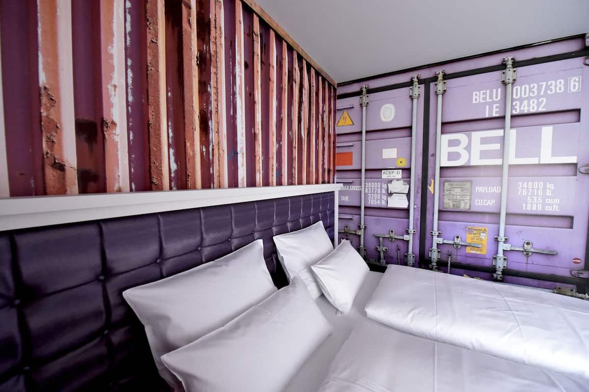 A bedroom with a bed, a headboard, and a wall with shipping containers.
