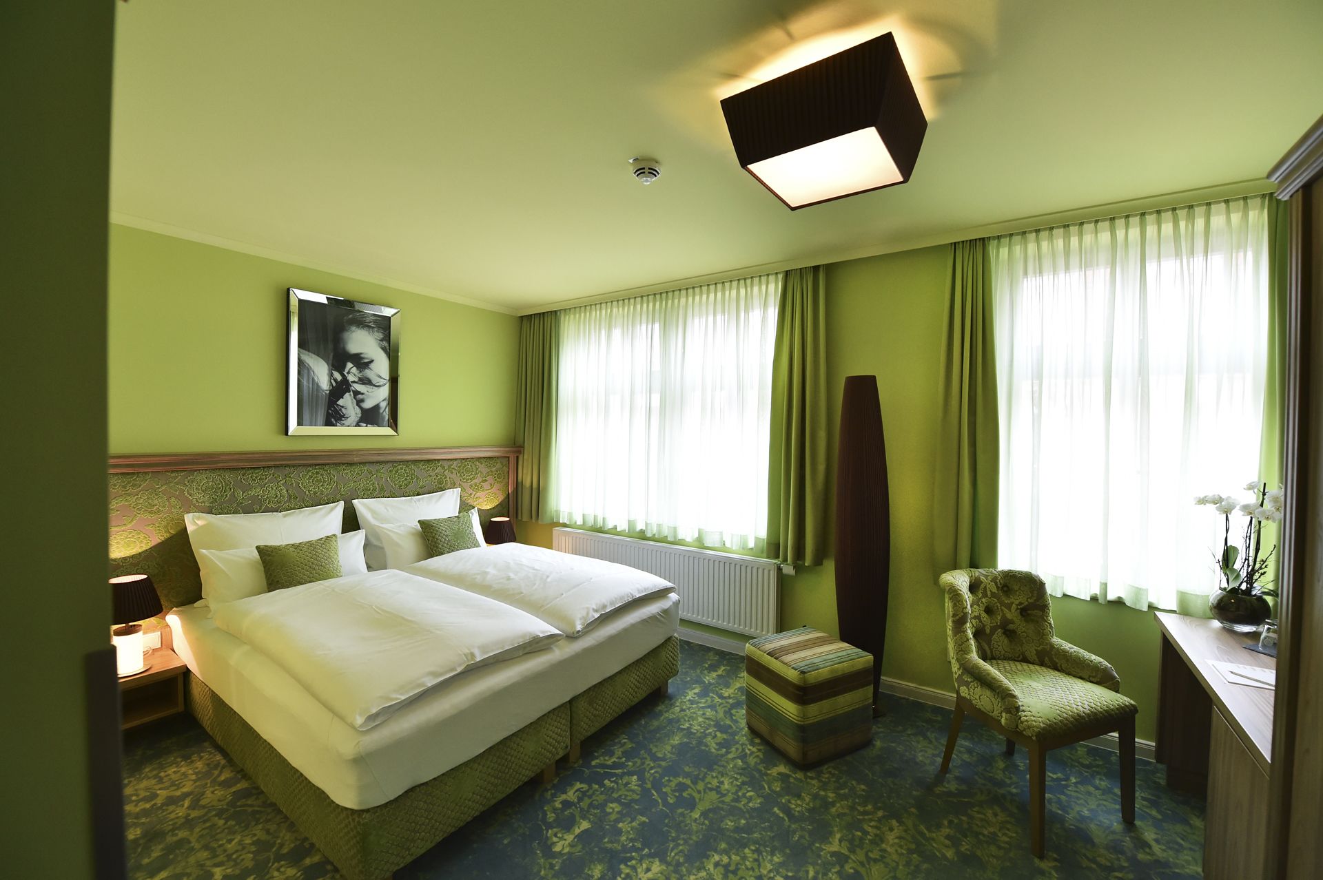 A hotel room with a large bed, a chair, a desk, and a window with curtains.