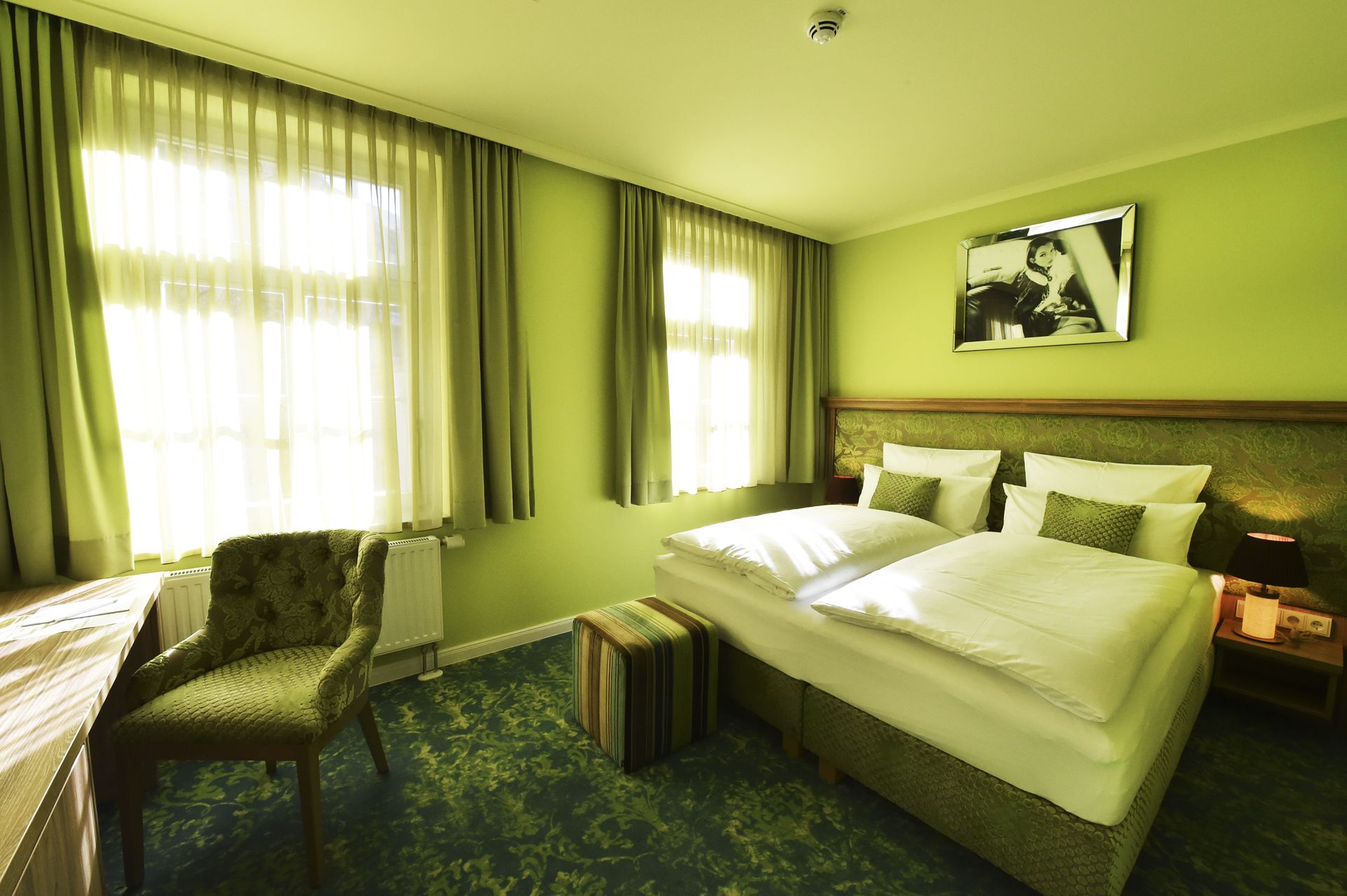 A hotel room with a bed, a chair, a bedside table, and a picture on the wall.