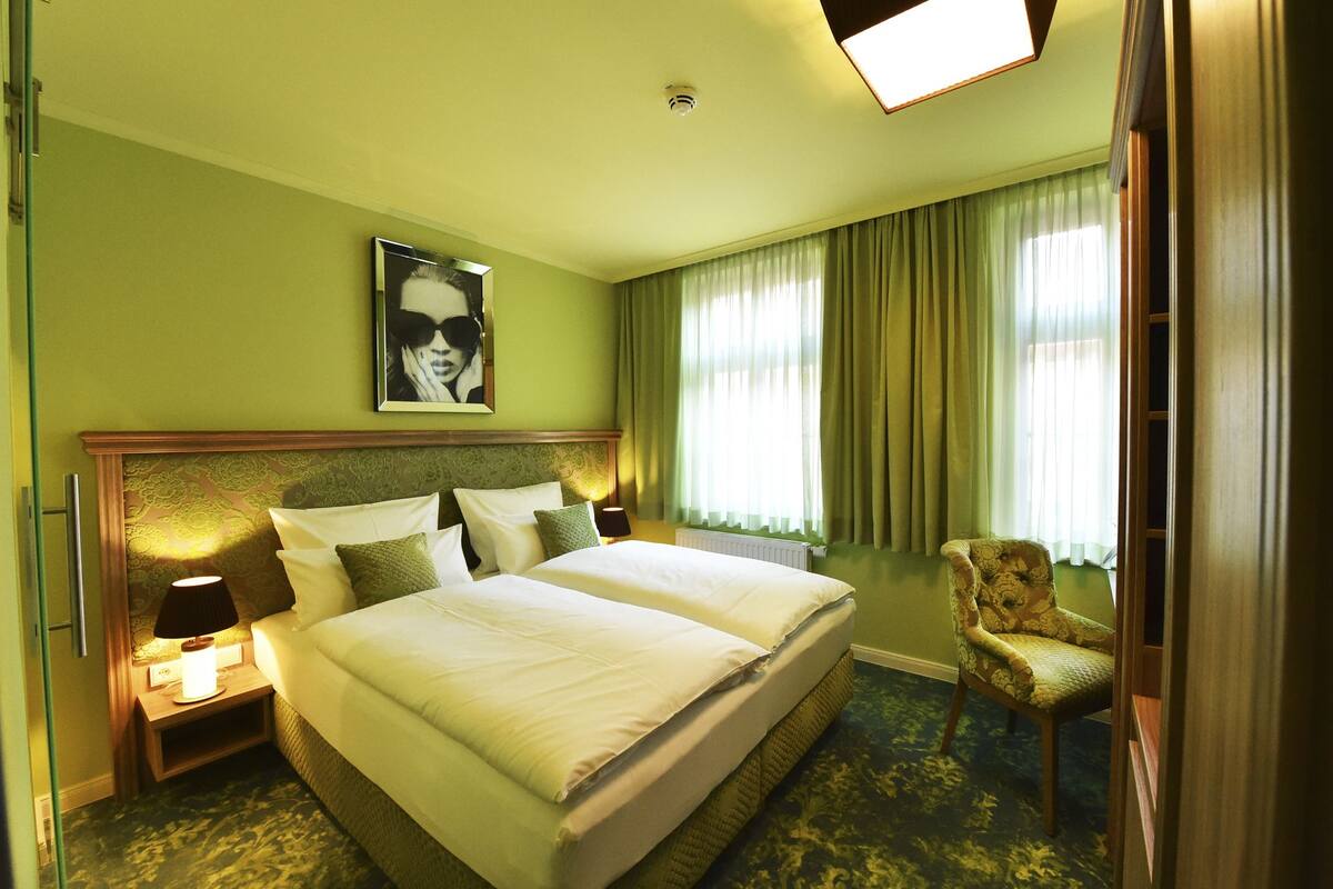 A hotel room with a large bed, two bedside tables, a chair, and a painting on the wall.