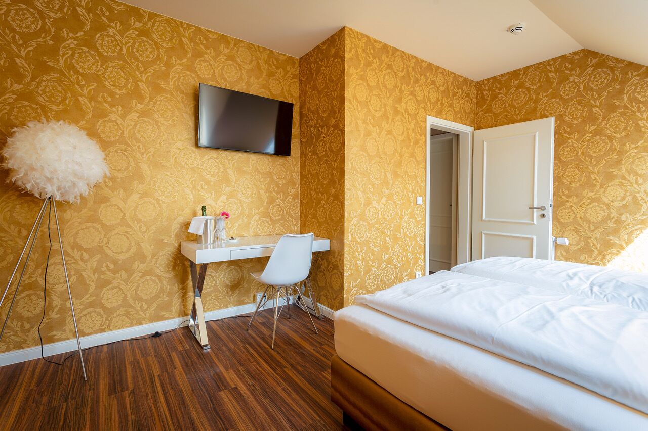 A hotel room with a bed, a desk with a chair, a television, and a door.