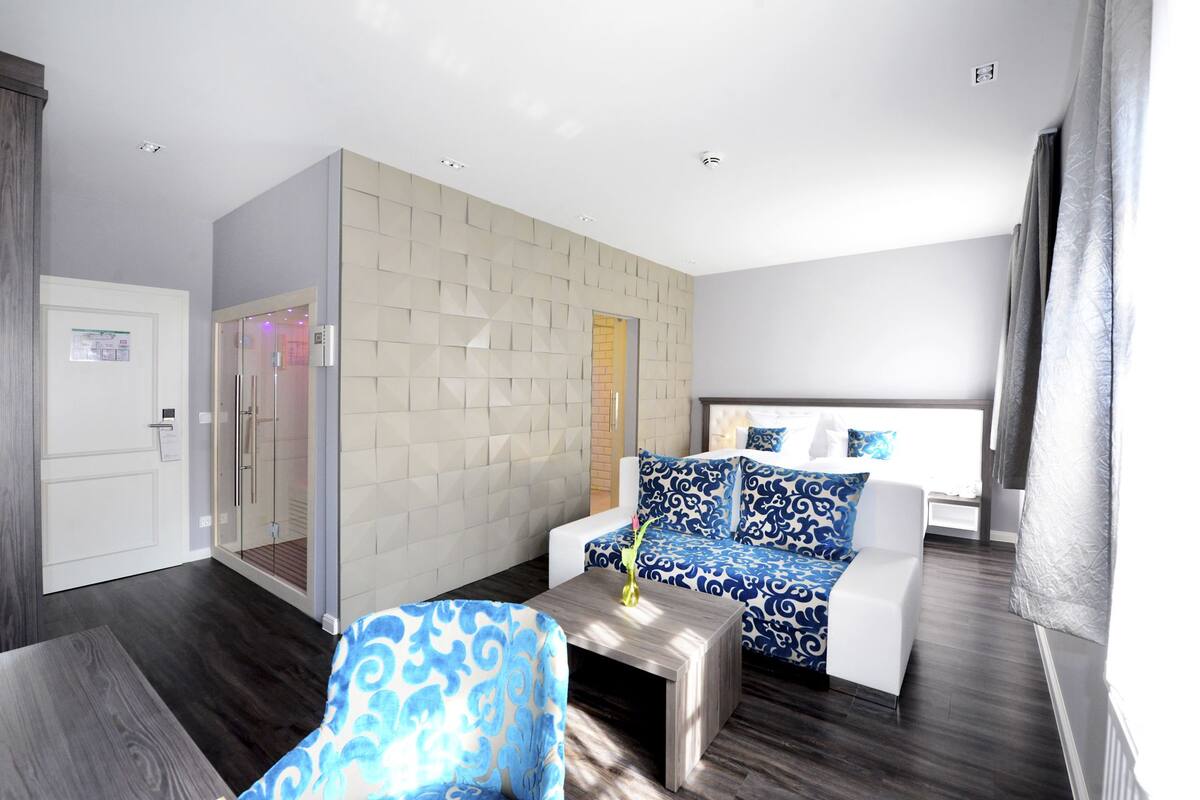 A modern hotel room with a large bed, a sofa, a coffee table, and a bathroom with a glass shower.