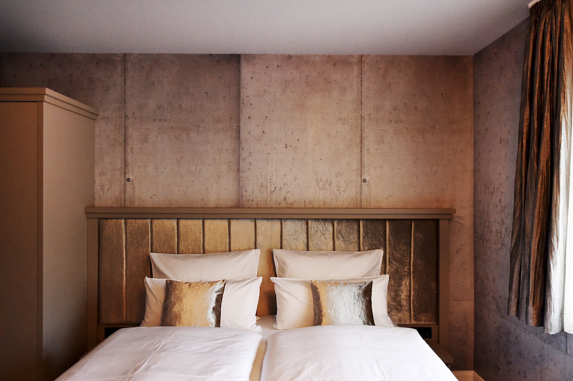 A hotel room with a wooden headboard, a large bed with white linens, and a curtain on the right side.