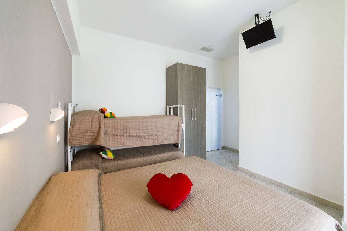 Una habitación con literas, un cojín rojo con forma de corazón y un televisor montado en la pared.