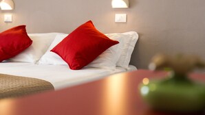 A neatly made bed with white linens and two red pillows.