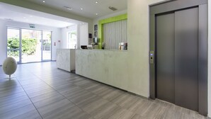 A modern reception area with a marble counter, a green accent wall, and a large elevator door.