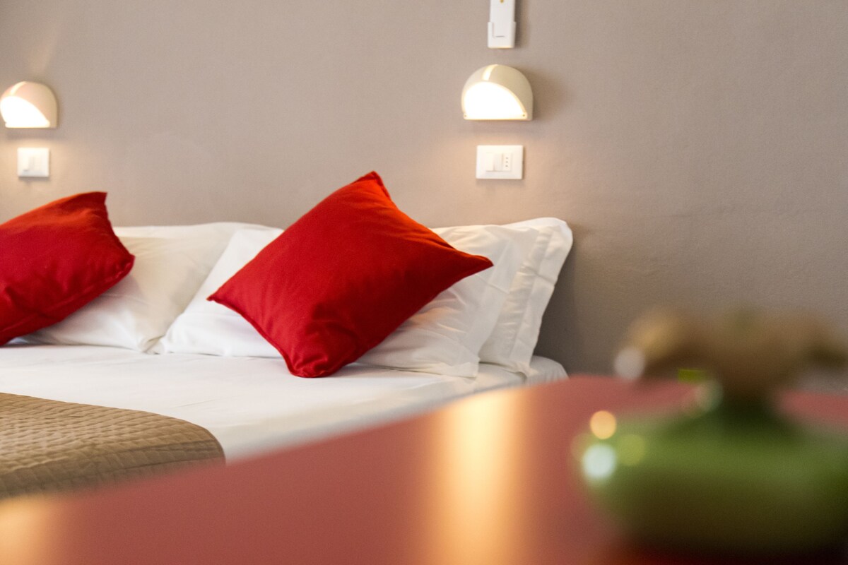 Habitación de hotel con cama, almohadas rojas e iluminación en la pared.