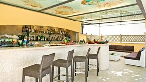 A bar area with wicker chairs, a counter with various bottles, and a ceiling mural.