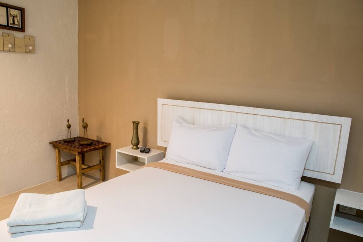 A hotel room with a large bed, a bedside table, a nightstand, and a wall-mounted shelf.