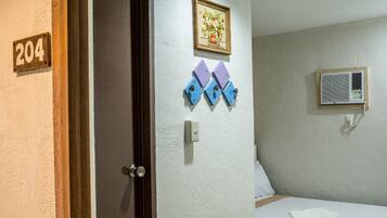 Habitación de hotel con una puerta que indica el número 204, una cama con almohada blanca, aire acondicionado montado en la pared y un cuadro enmarcado sobre la cama.